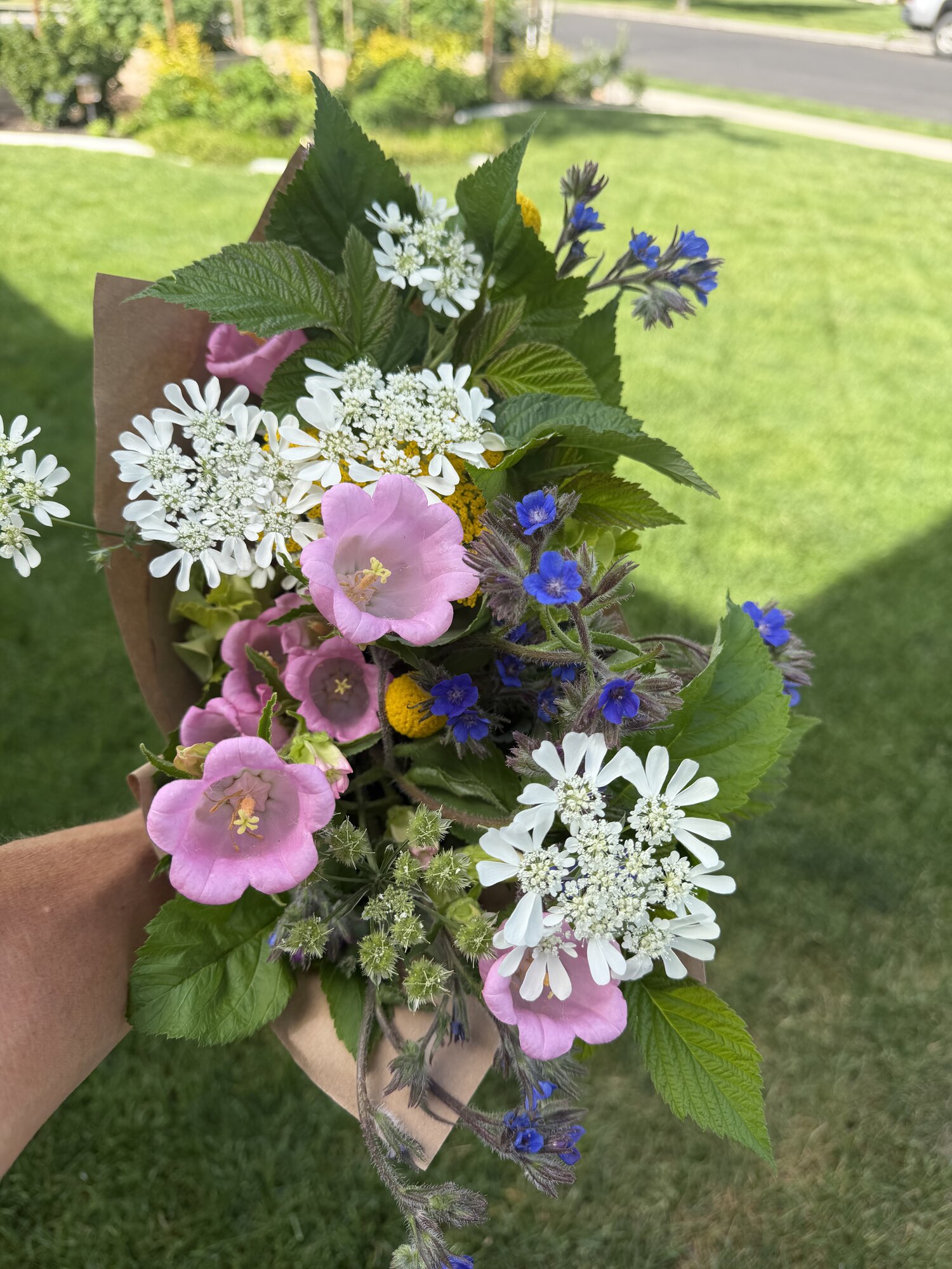 Hands wrapping a fresh bouquet of pink roses and lavender stock in kraft paper.